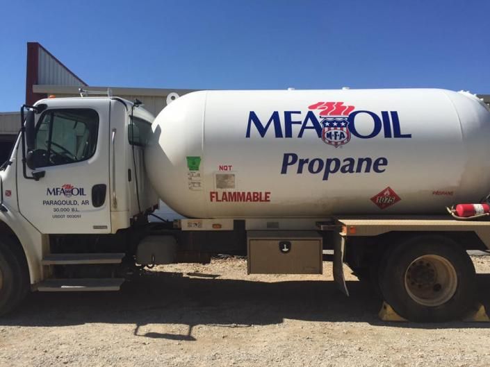 A white MFA Oil propane delivery truck parked on a gravel lot under a clear blue sky.