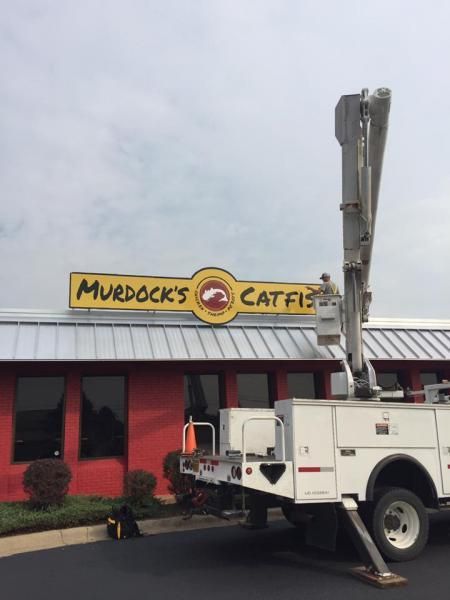 A white utility truck with an extended bucket lift parked in front of a red building with a Murdock's Catfish sign.
