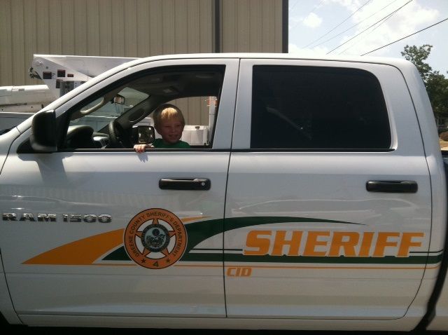 A person sitting in the driver's seat of a white Ram 1500 sheriff truck.