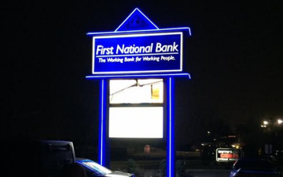 A brightly illuminated First National Bank sign glowing blue against a dark night background.