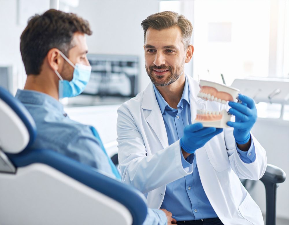 Dentist showing dental model to patient. Both are in a dental office. Patient wearing a mask.