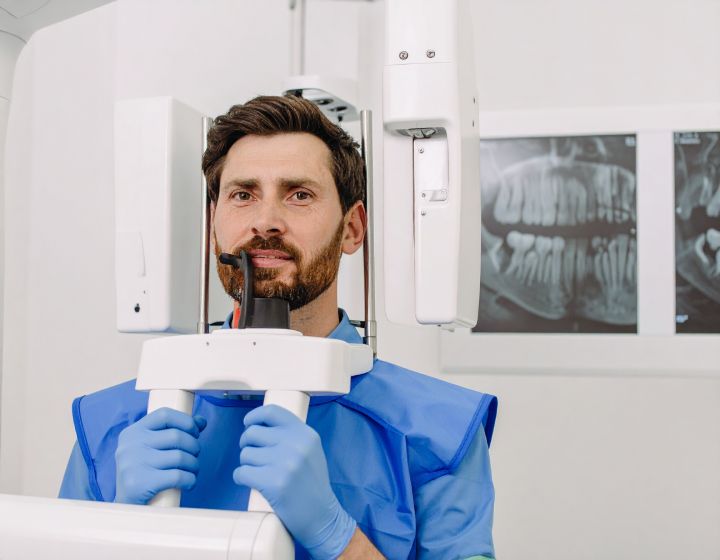 Man in dental bib using panoramic X-ray machine.