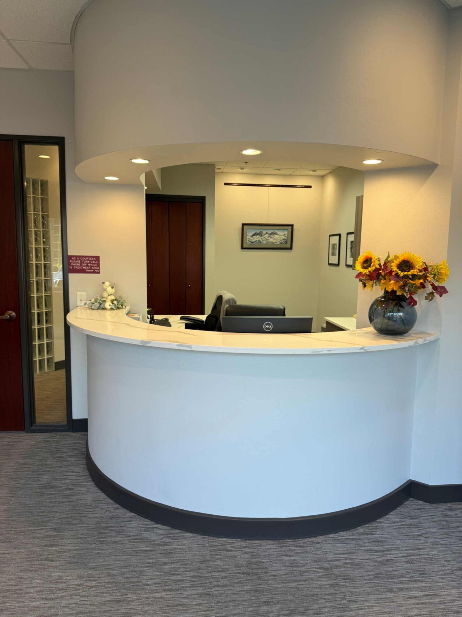 Reception desk in a professional office. Curved white counter with vase of flowers, backdrop of office interior.