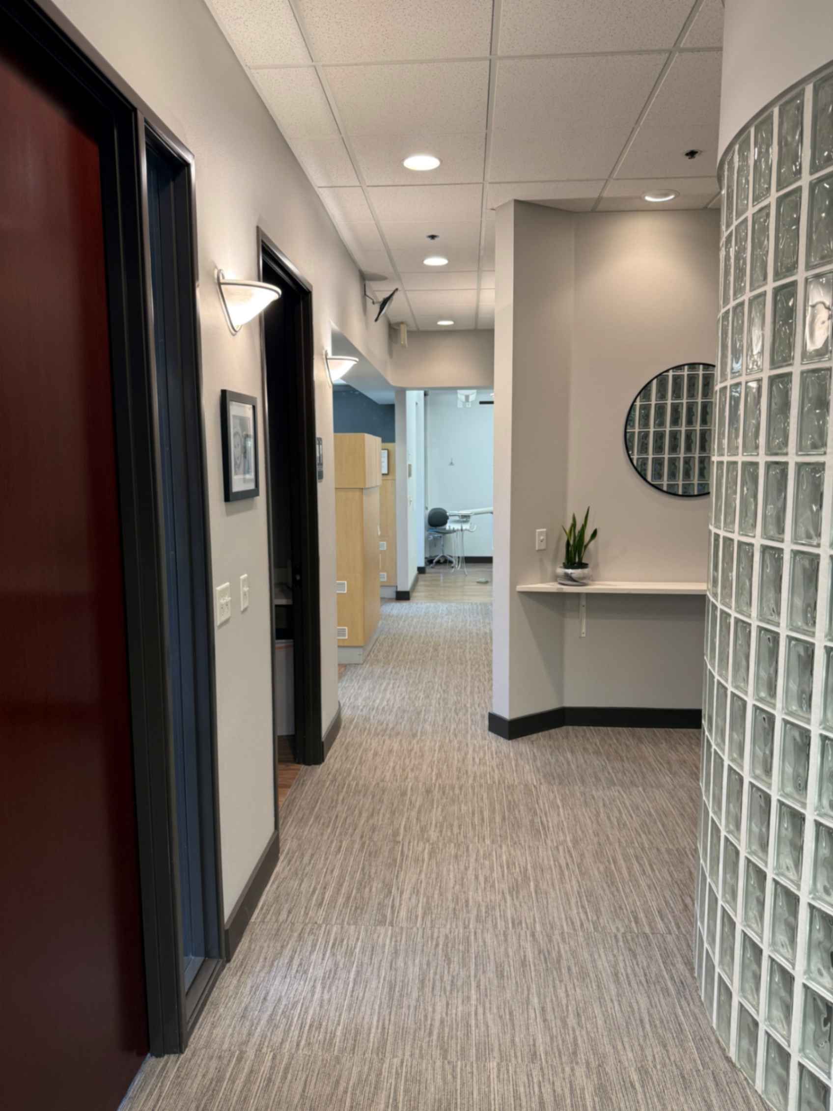 Long hallway in a building with doors on the left, a glass block wall on the right, and a waiting area at the end.