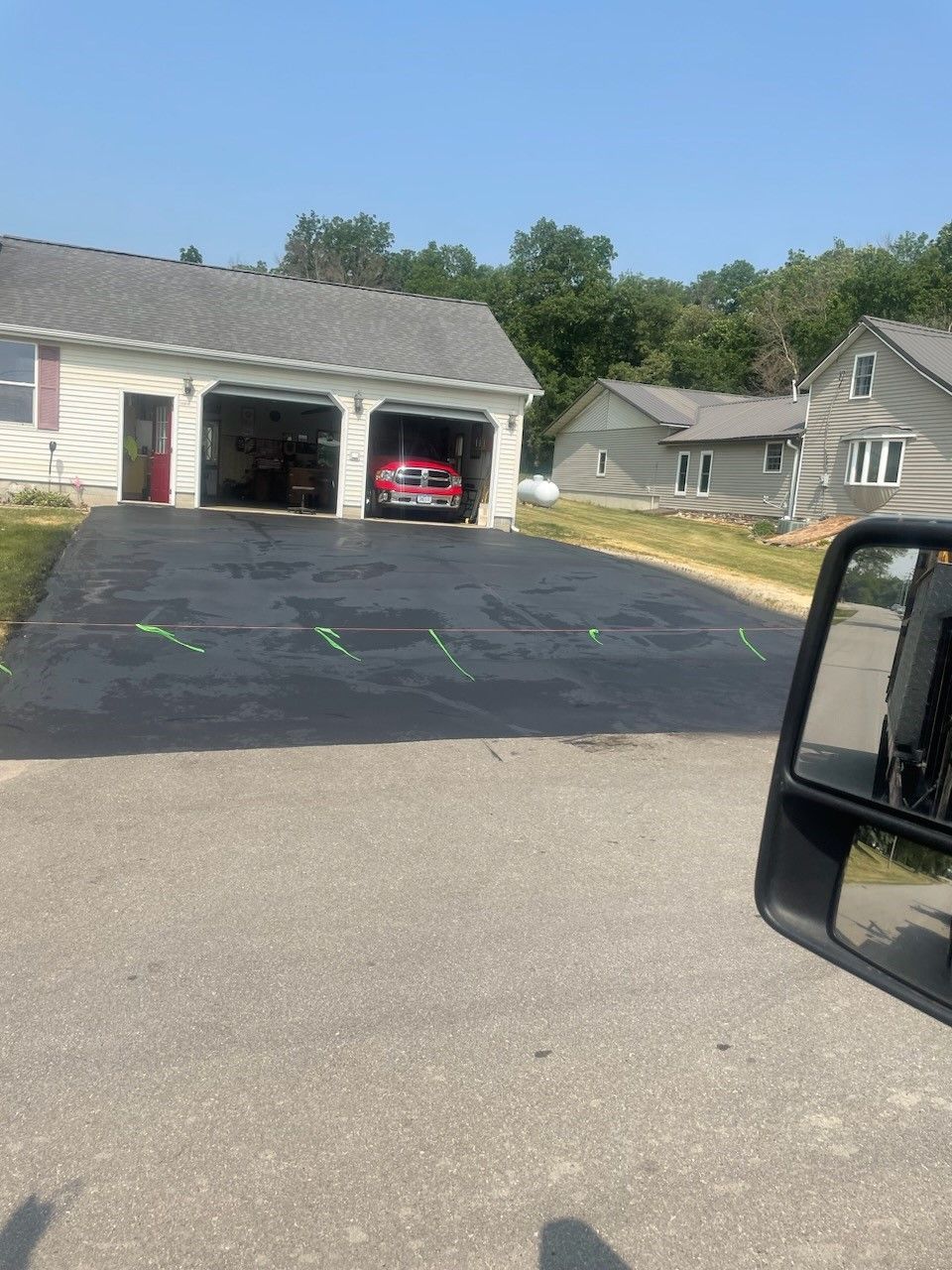 Driveway in front of a garage with a red SUV parked inside, beside a residential street on a sunny day.