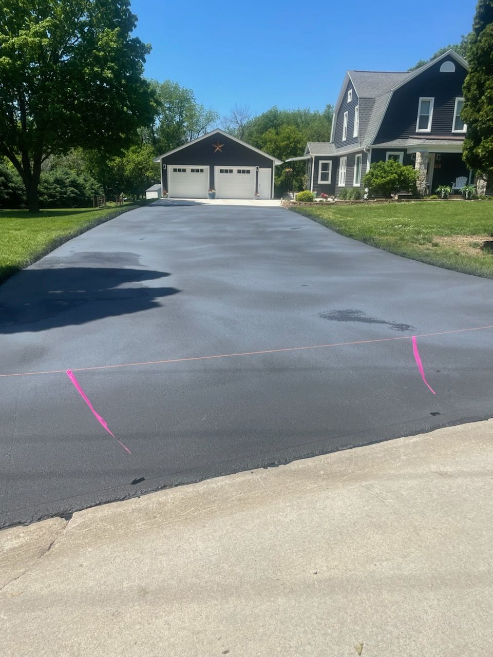 Fresh black asphalt driveway leading to a white garage and house under a blue sky