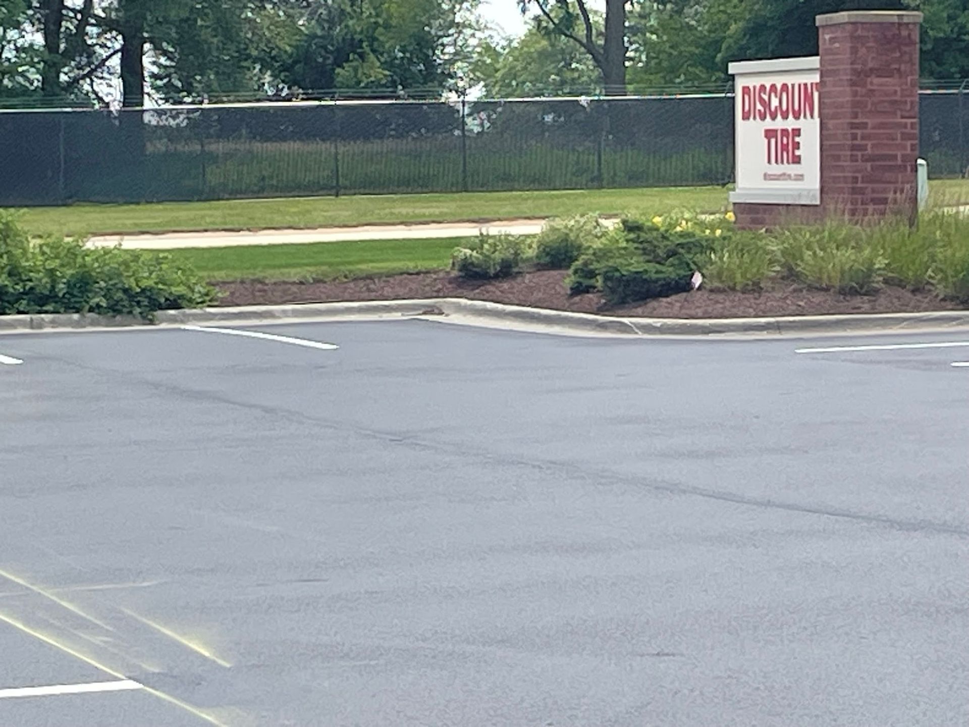 Empty parking lot with a brick sign reading “DISCOVER THE” beside a grassy roadside.