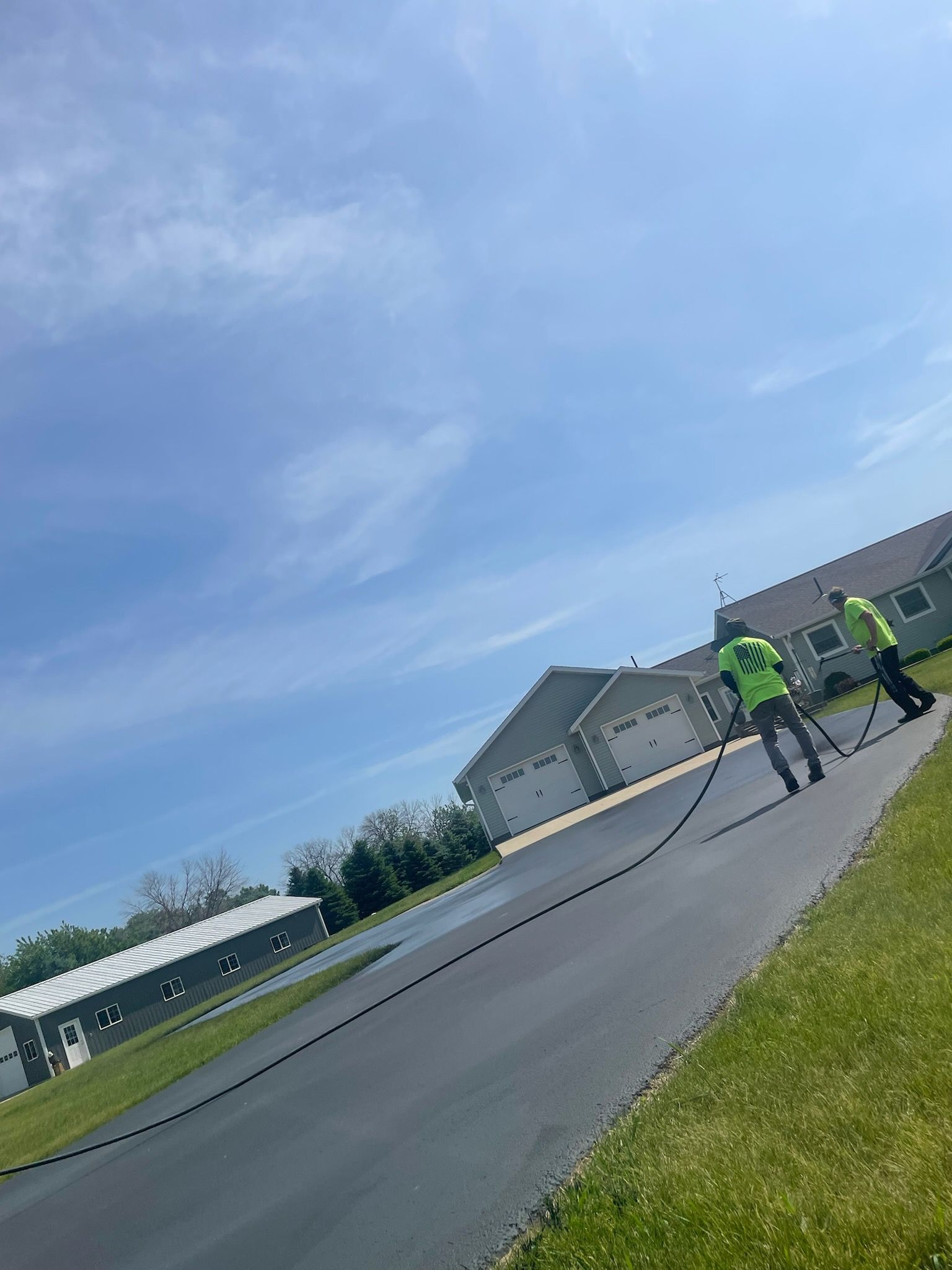 Two workers in neon safety vests on a roadside near houses under a cloudy sky