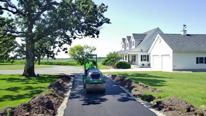 Freshly paved driveway leading to a white house, with a green ATV parked in the center.
