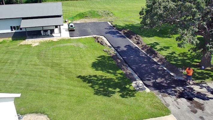 Aerial view of a house, green lawn, and long driveway with one person in an orange shirt near the road.