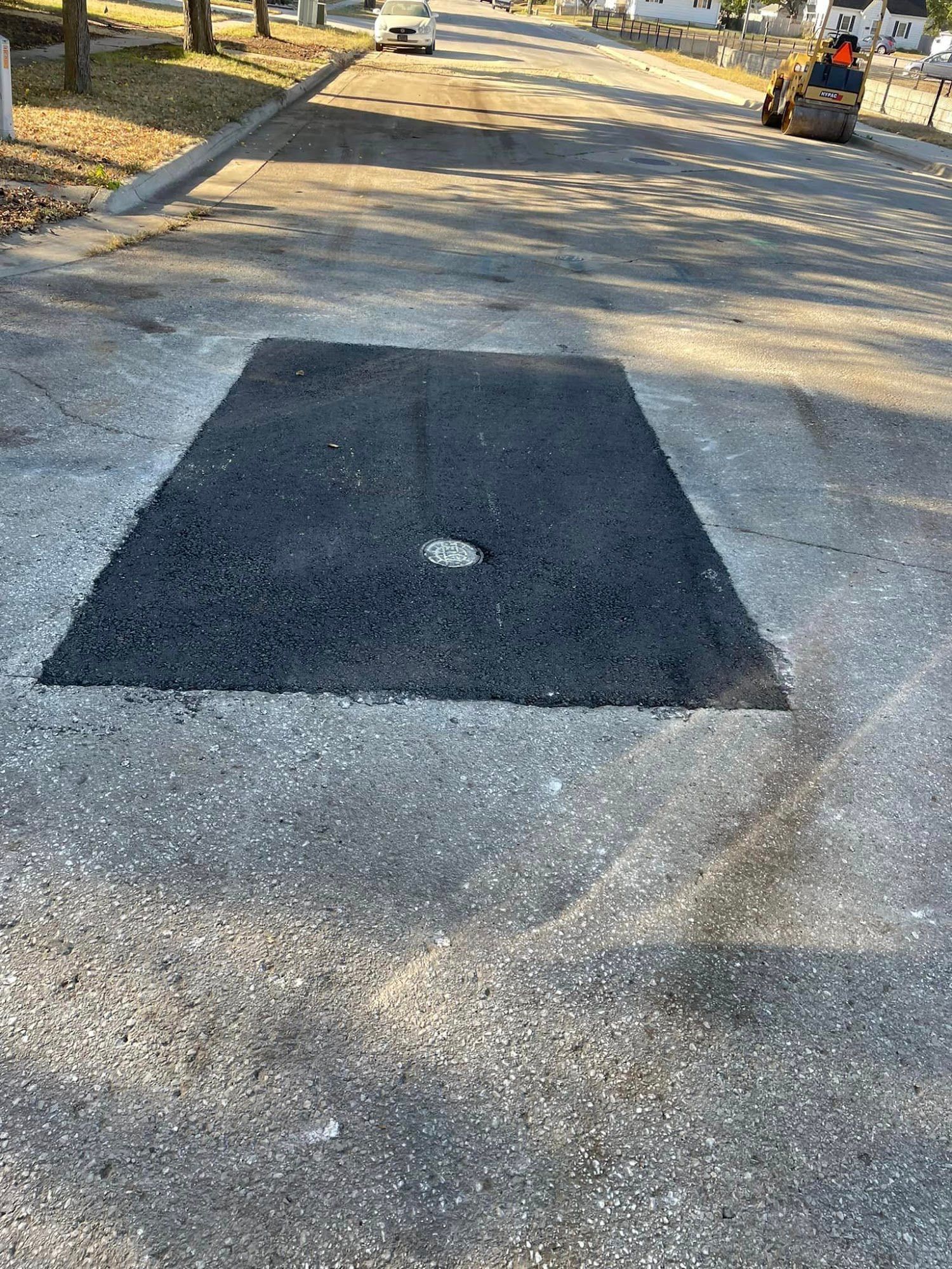 Fresh black asphalt patch in a paved area, with a small circular drain or hole at the center.