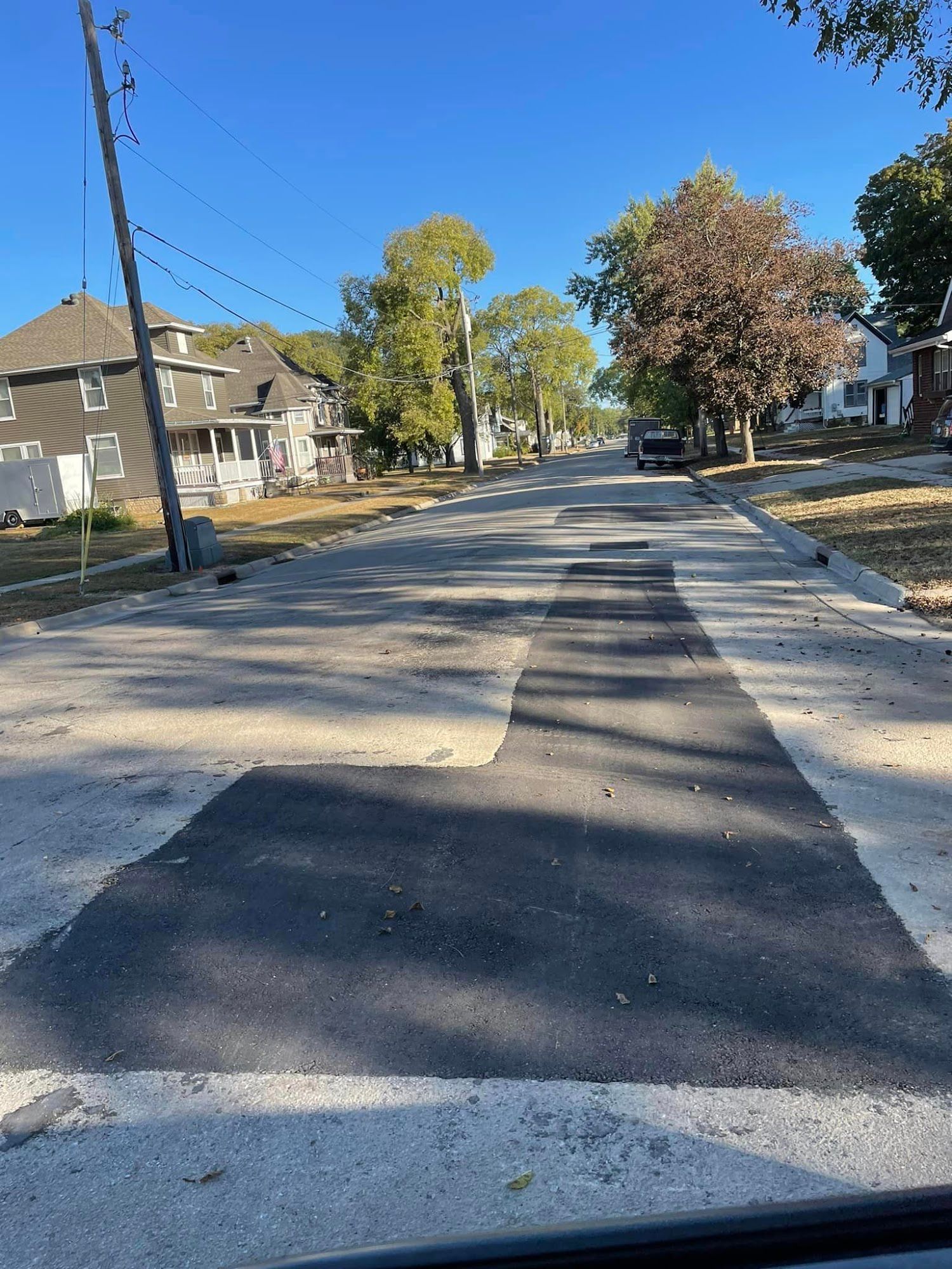 Residential street with fresh black asphalt patches, trees, and houses on a sunny day