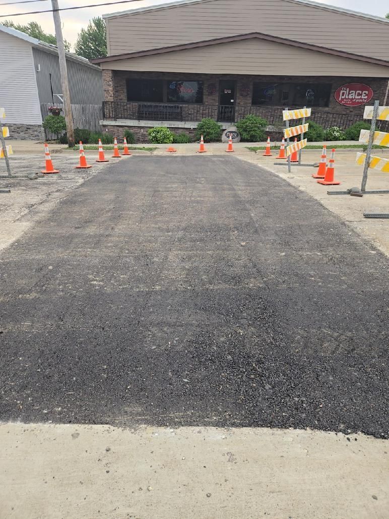 Freshly paved driveway with orange cones and barricades leading to a building entrance