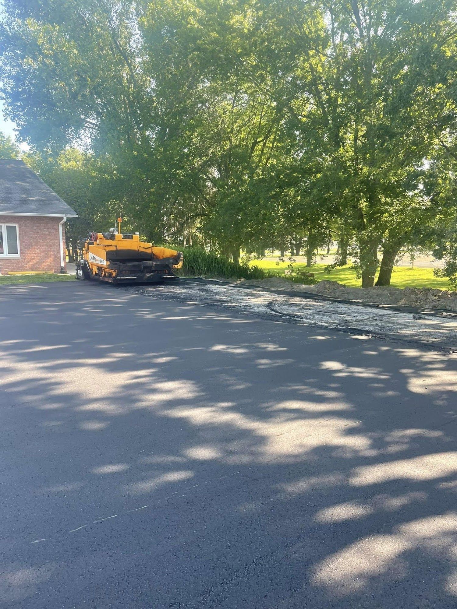 Orange car parked by a brick house on a tree-lined driveway, with sunlight and shadows on the pavement