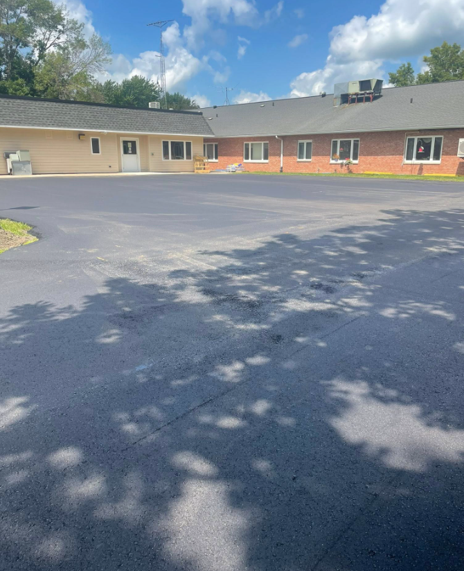 Single-story brick building with a large empty asphalt lot under a partly cloudy sky