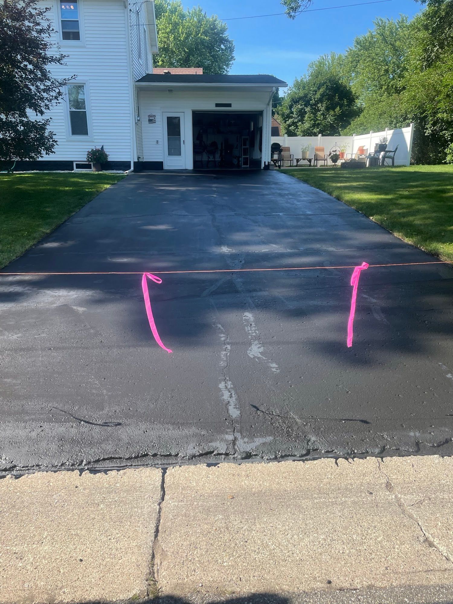 Driveway in front of a house, with two pink chalk marks on the asphalt near the curb.