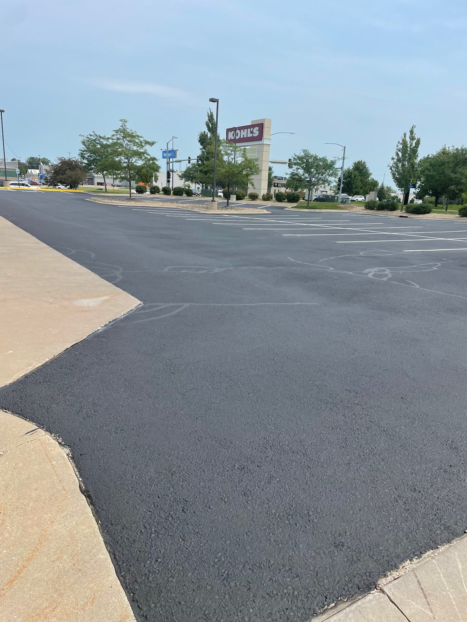 Empty parking lot with dark asphalt, concrete curb, and a shopping center sign under a clear blue sky