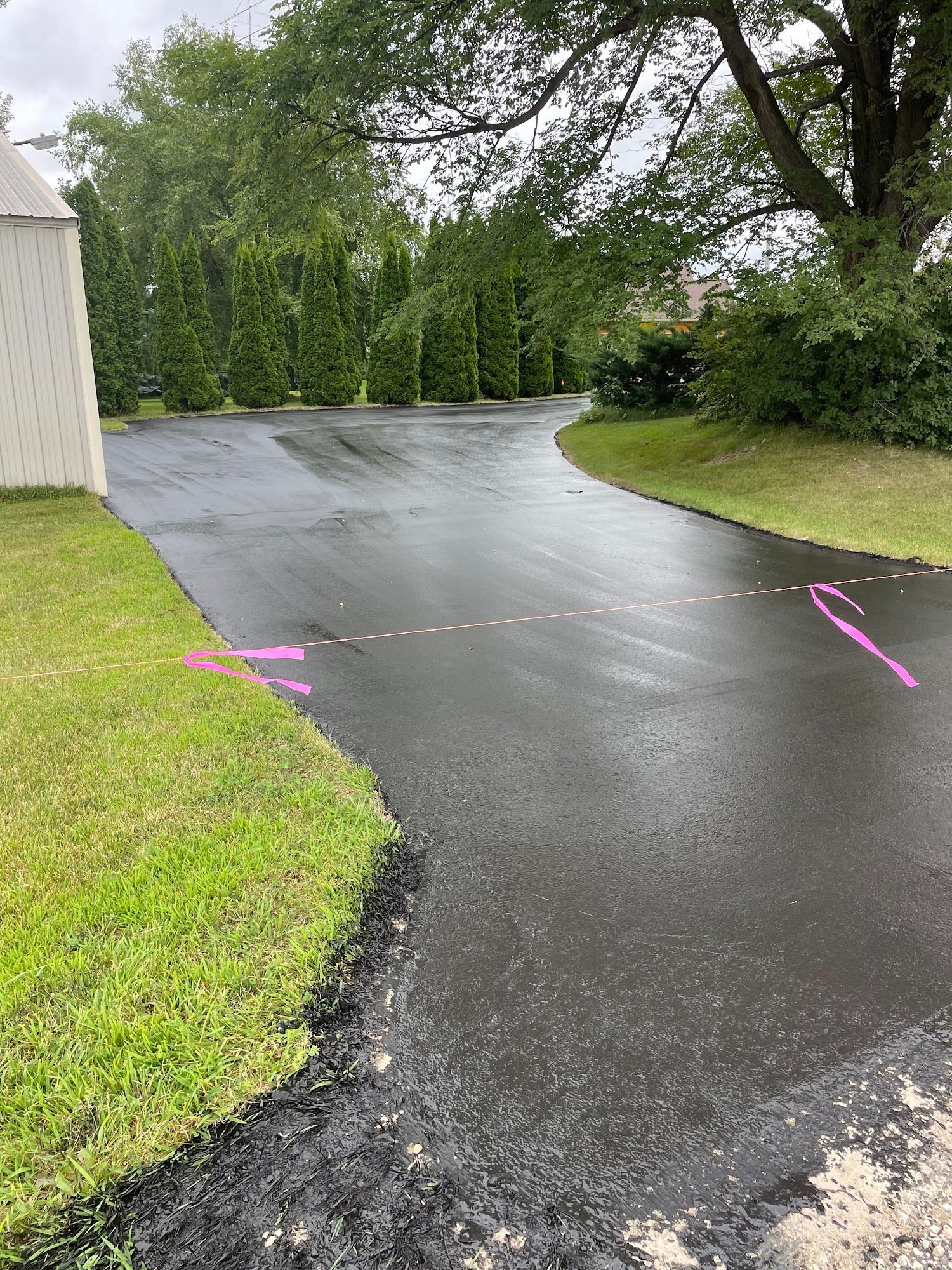 Wet black driveway curving through a green yard beside a light-colored building