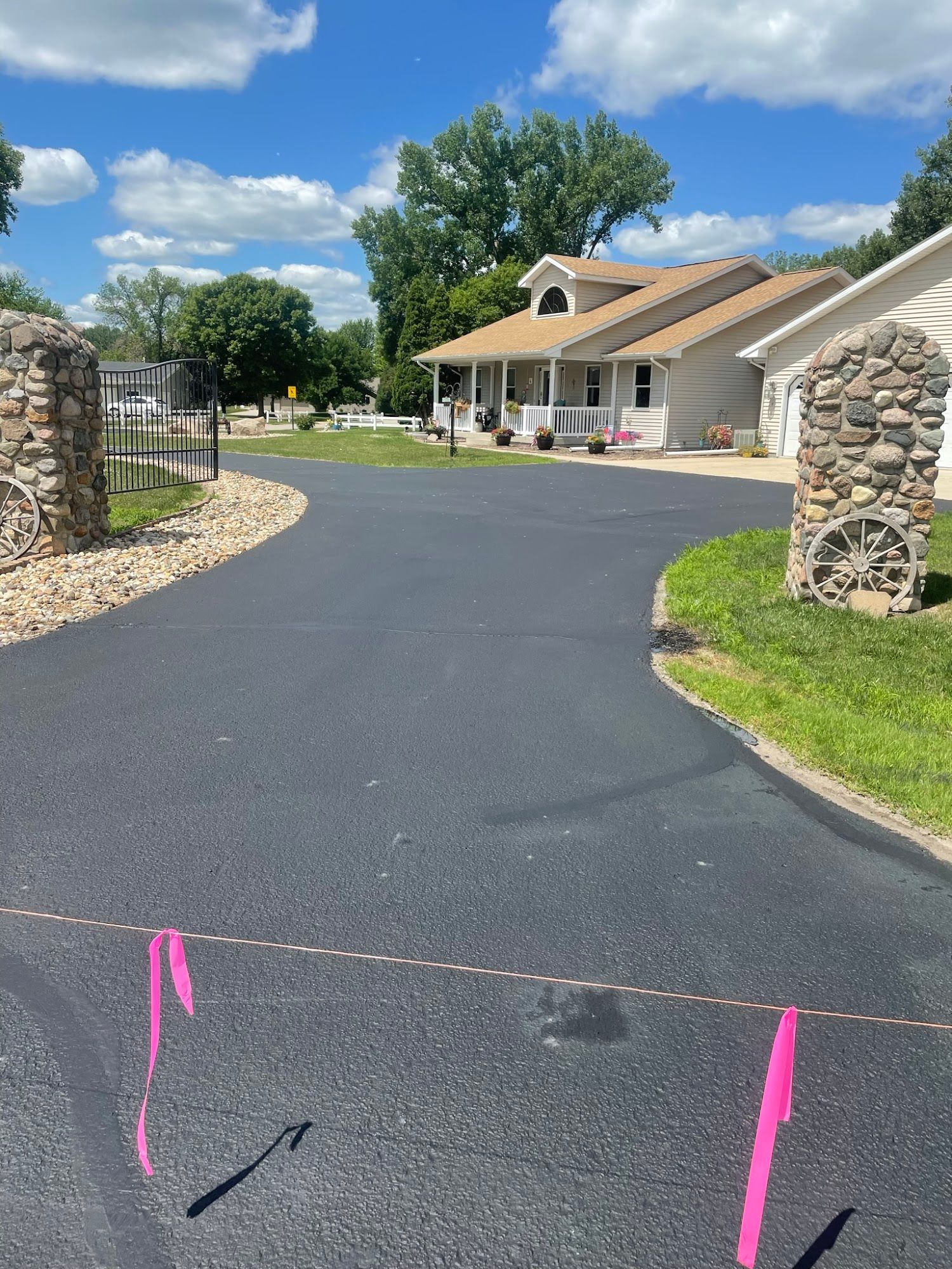 Freshly paved driveway leading to a building entrance between stone pillars under a blue sky