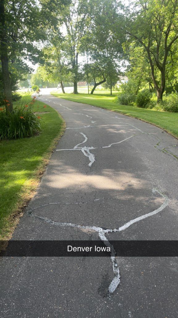 Cracked asphalt path through a green park with trees and sunlight