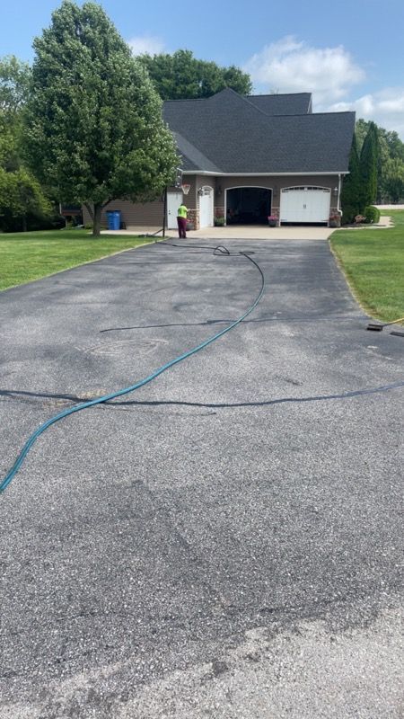 Suburban house with open garage viewed from a long asphalt driveway on a sunny day