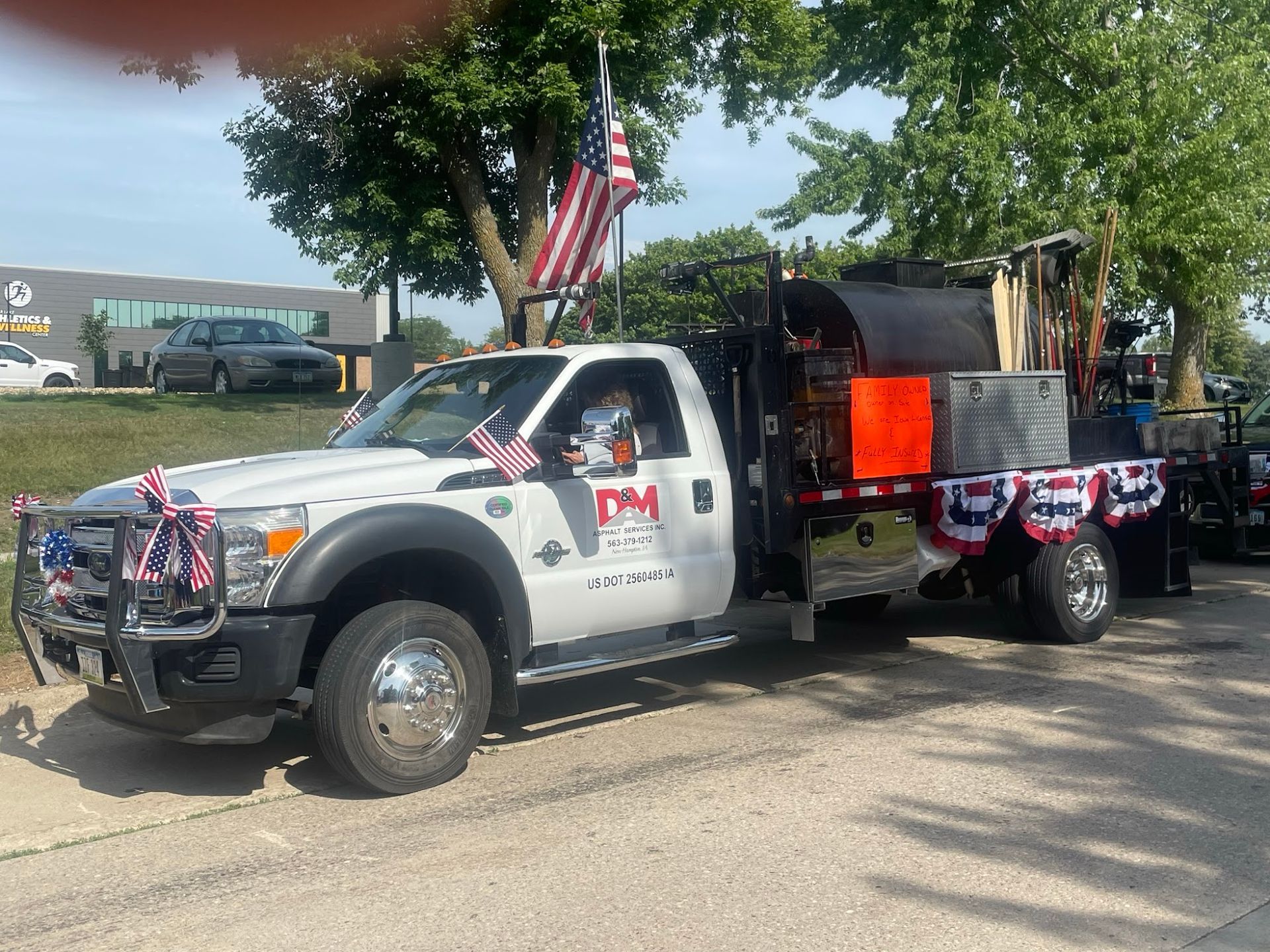 Decorated white truck with flag and equipment parked on a sunny street during a parade