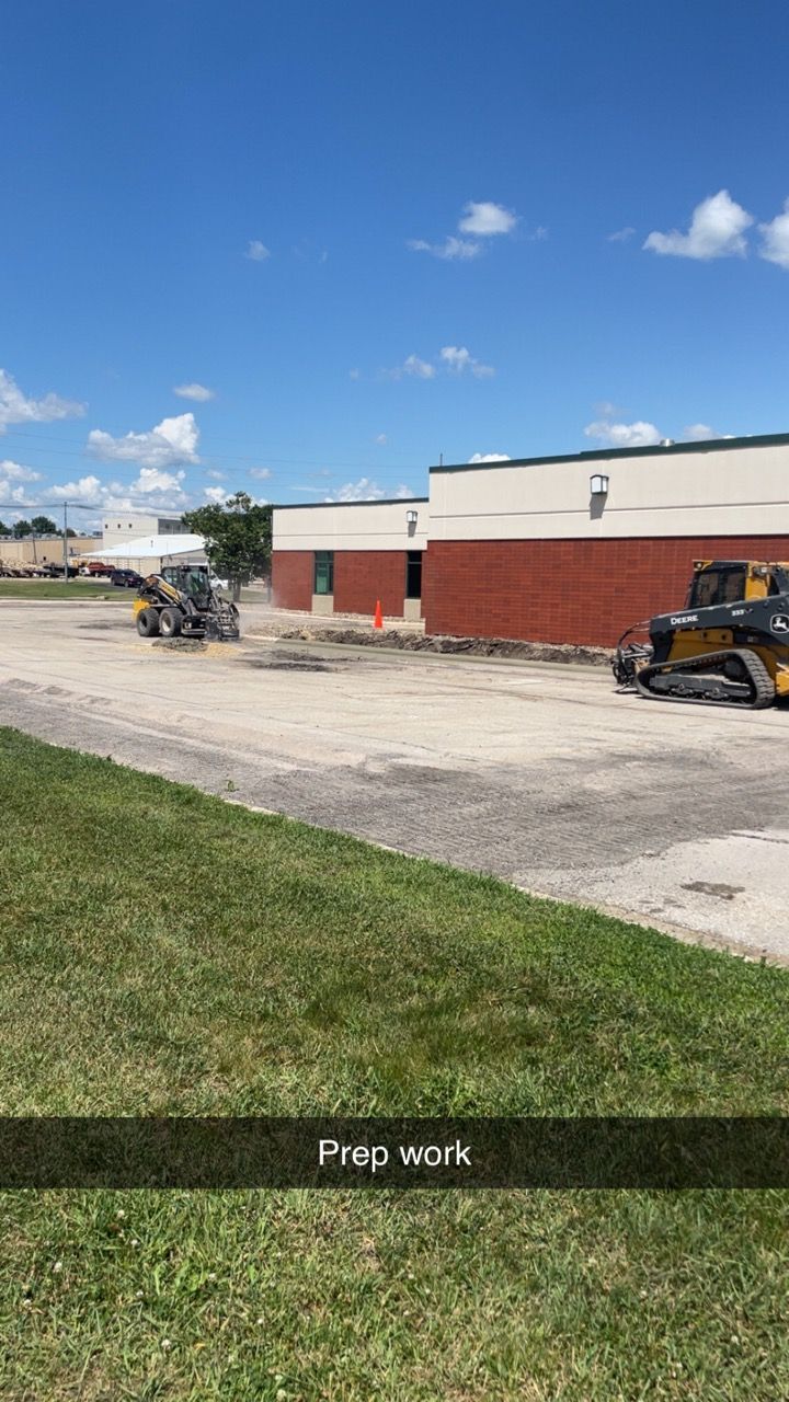 Gravel lot beside a red-and-white building under a blue sky, with a small excavator on the right.