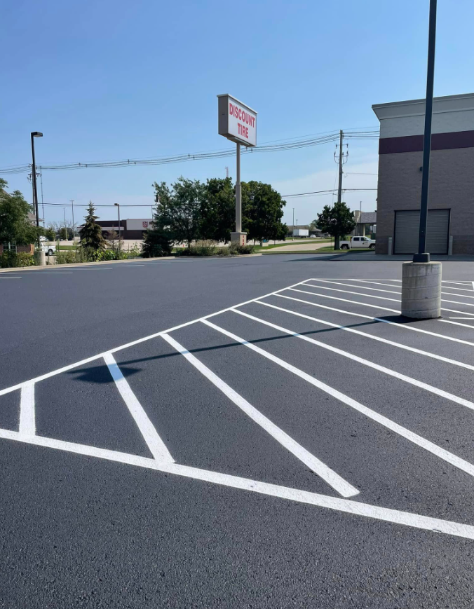 Empty parking lot with white diagonal lines and a store sign in the background under a clear sky