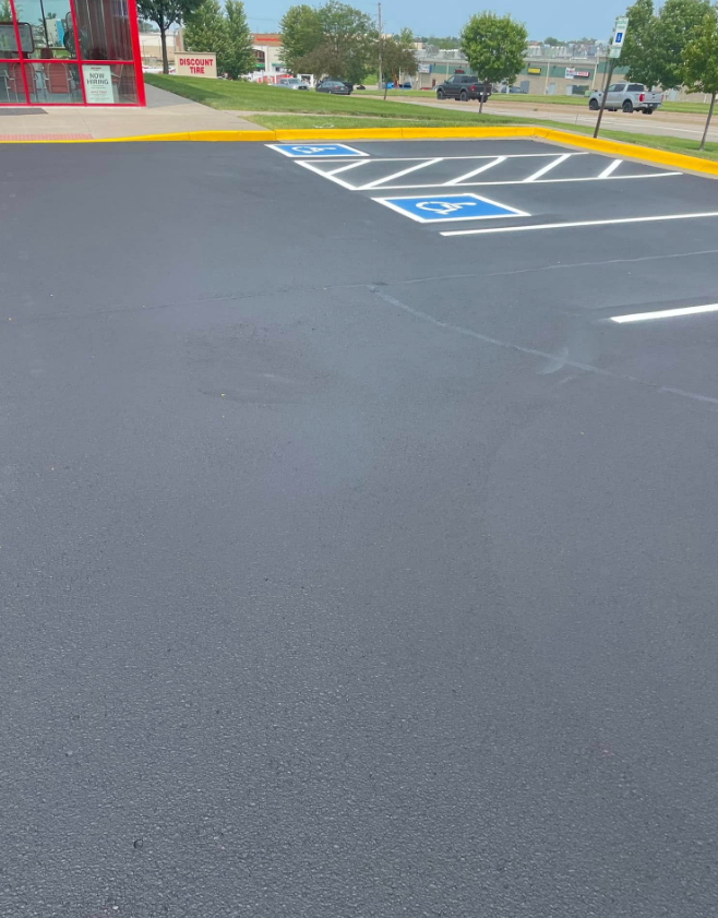 Empty accessible parking spaces on a freshly paved lot beside a red storefront.