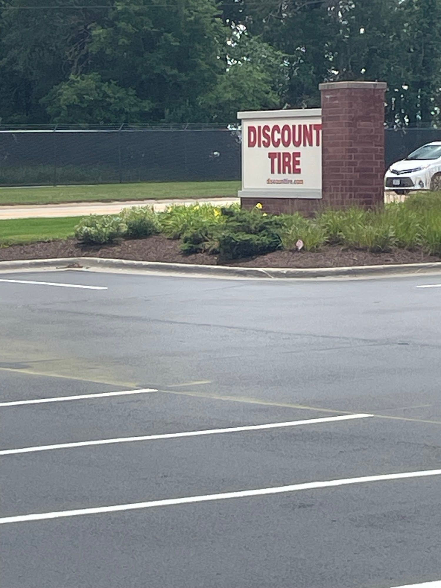 Discount Tire sign by a parking lot and brick pillar, with a parked car in the background.