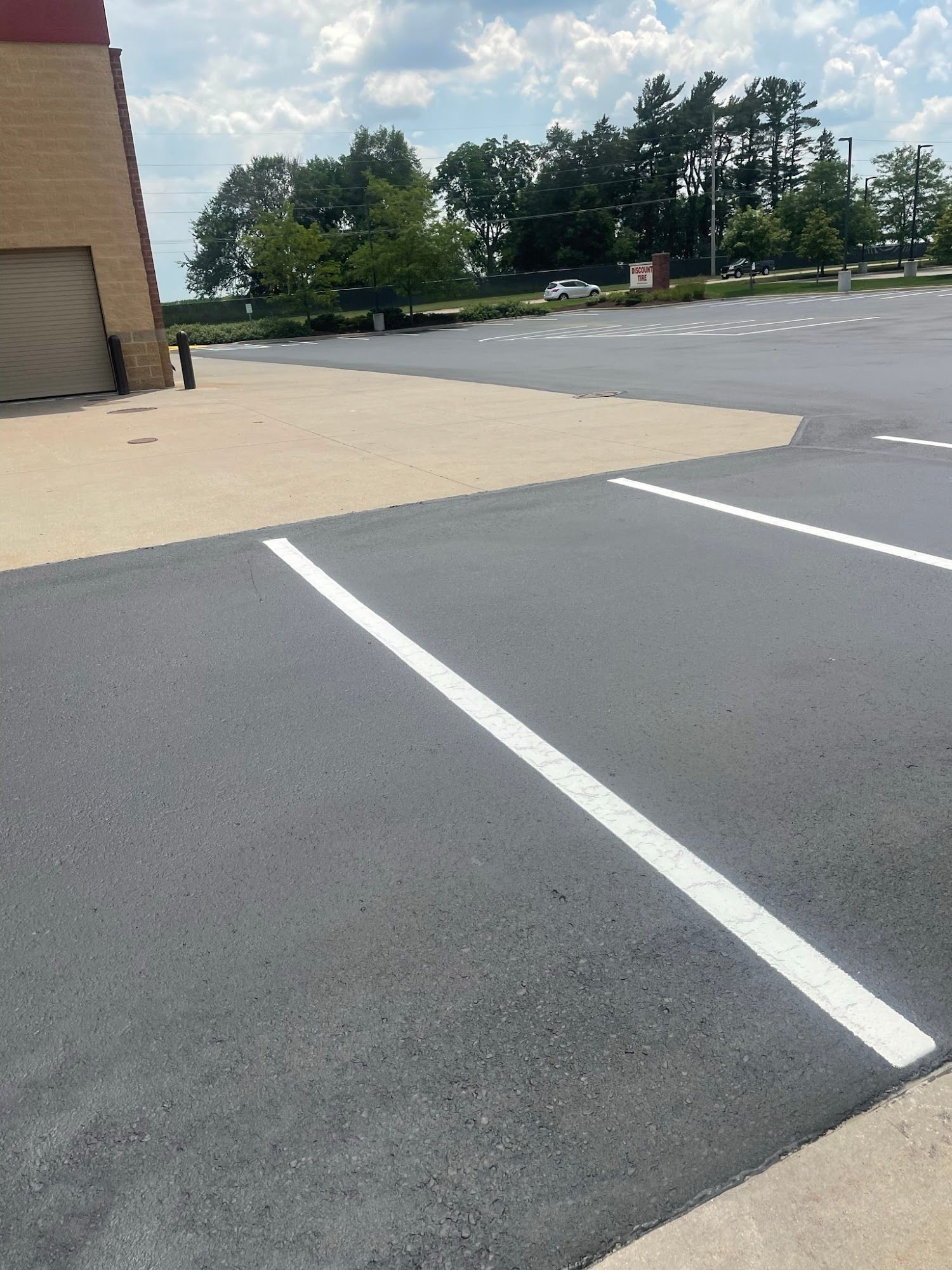 Empty parking lot with white space lines beside a beige building and trees in the distance
