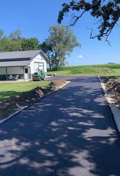 Freshly paved driveway leading to a white house on a sunny rural property