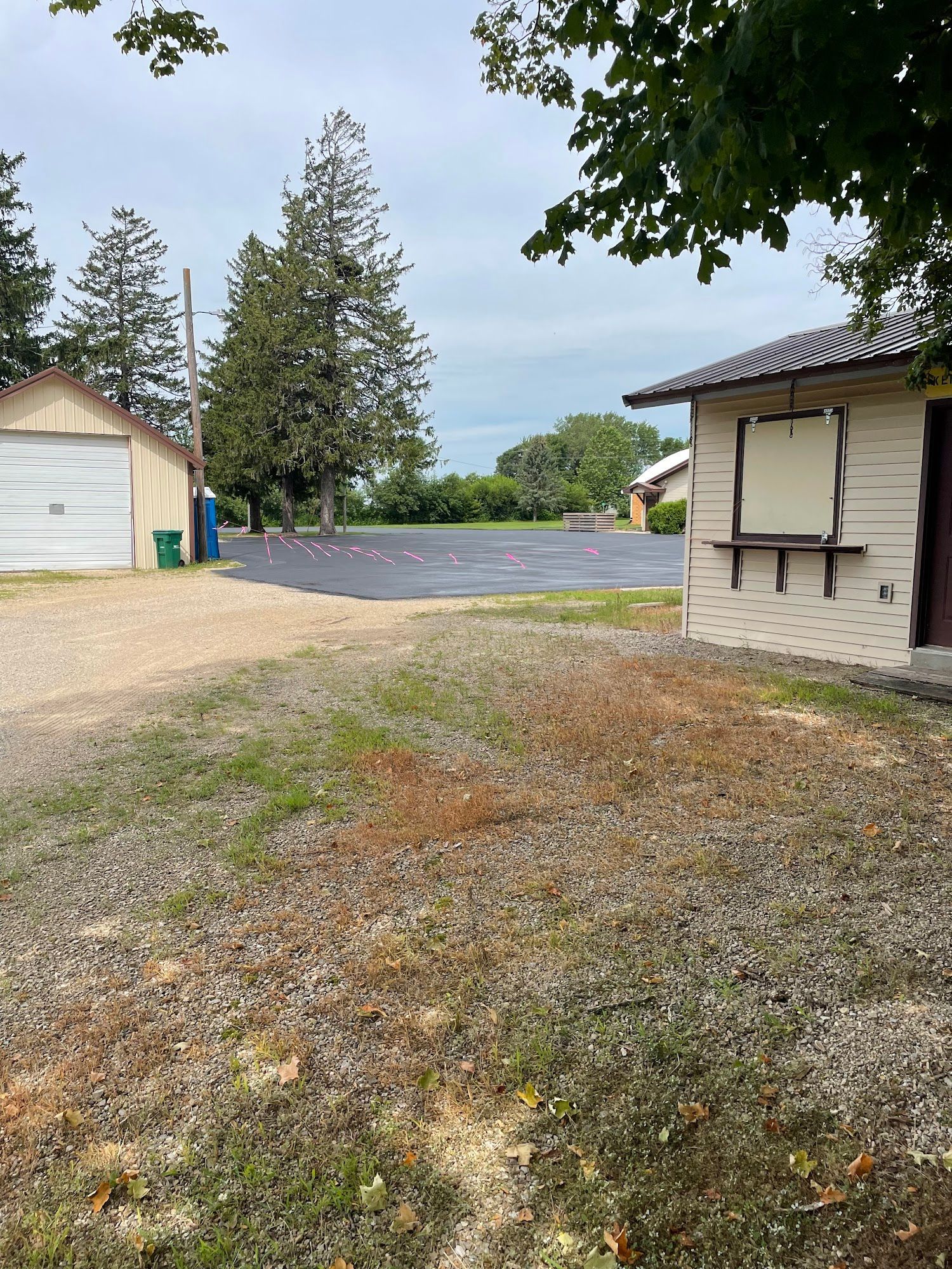 Gravel driveway beside a white garage and house, opening to a road with trees and cloudy sky.