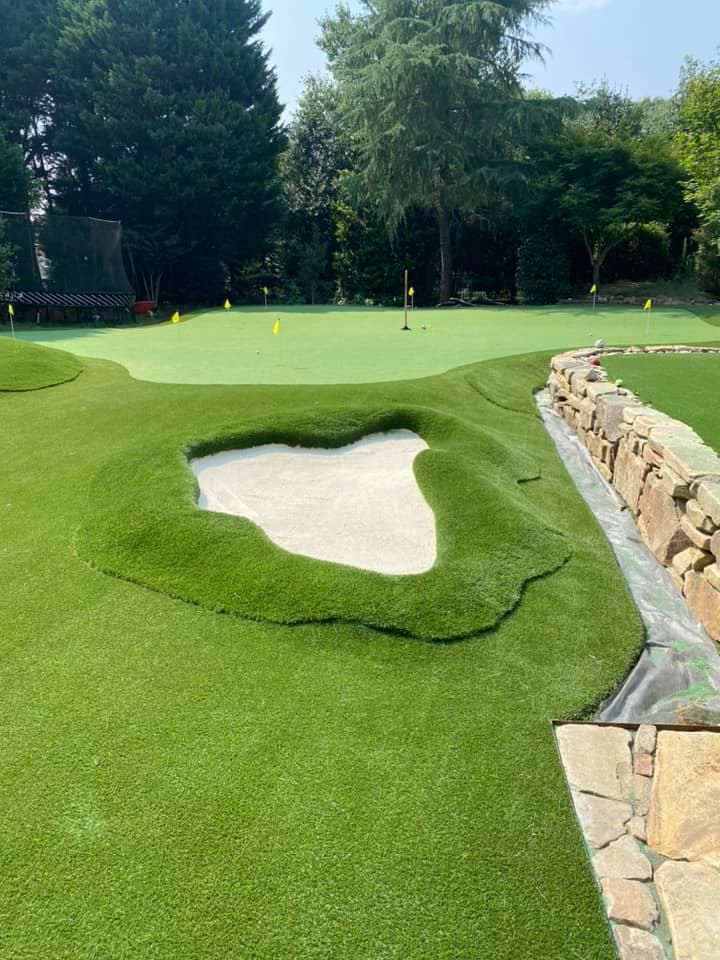 Miniature golf course with green turf, a sand trap, and a stone wall.