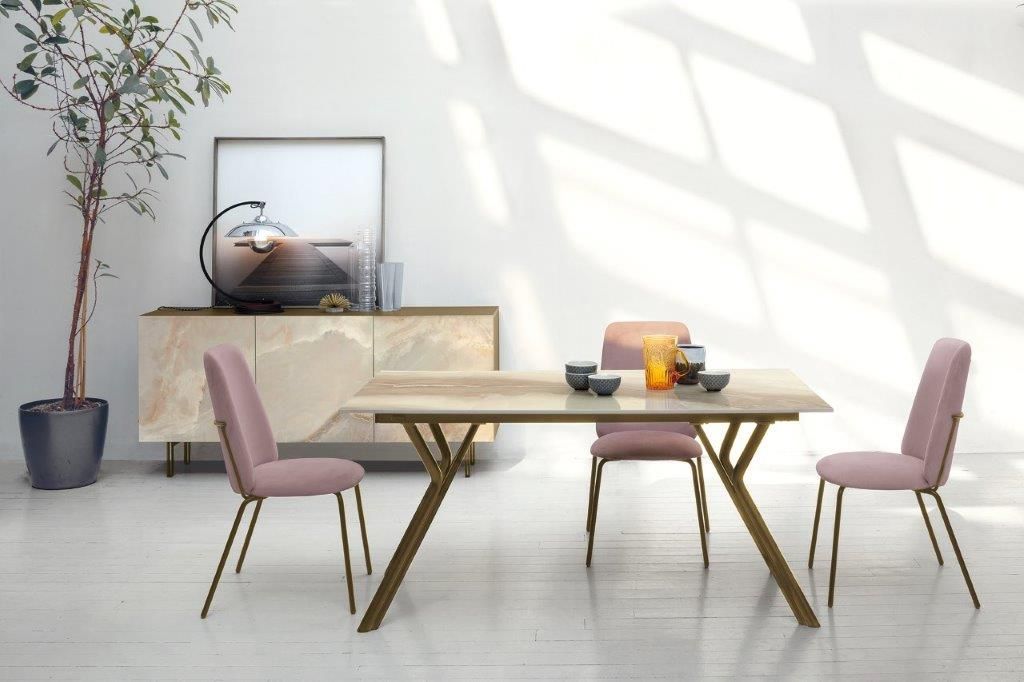 Sala da pranzo con sedie rosa, tavolo effetto marmo e credenza, contro una parete bianca con ombre solari.
