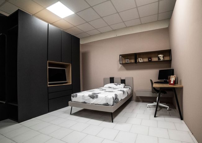 Camera da letto con armadio, letto, scrivania e scaffali grigio scuro. Pareti rosa, pavimento bianco.