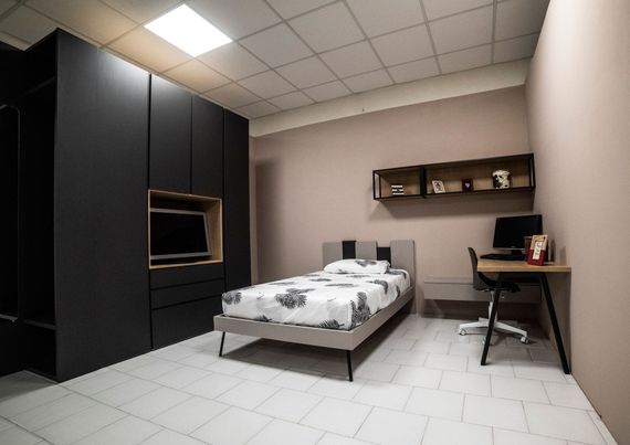 Camera da letto con armadio, letto, scrivania e scaffali neri; pareti e pavimento chiari.