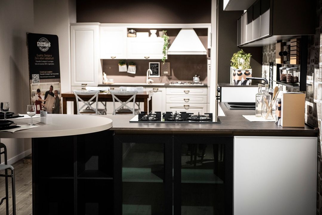 Cucina con isola, mobili scuri, piano cottura a gas, ripiani bianchi e altri mobili sullo sfondo.