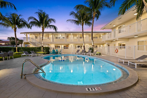 A large swimming pool surrounded by palm trees in front of a hotel.