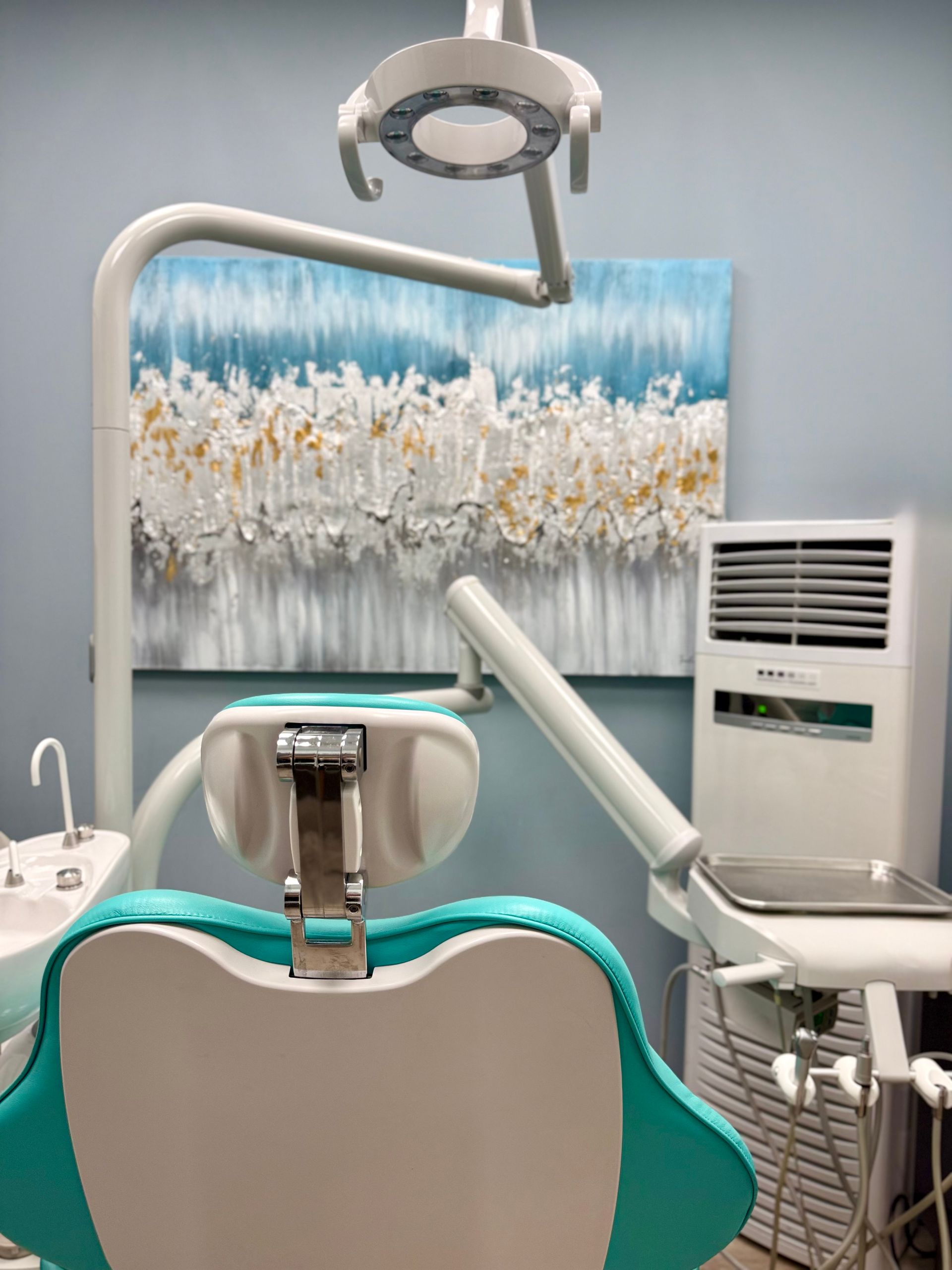 Dental exam room with chair, overhead lamp, and wall art in blue and white