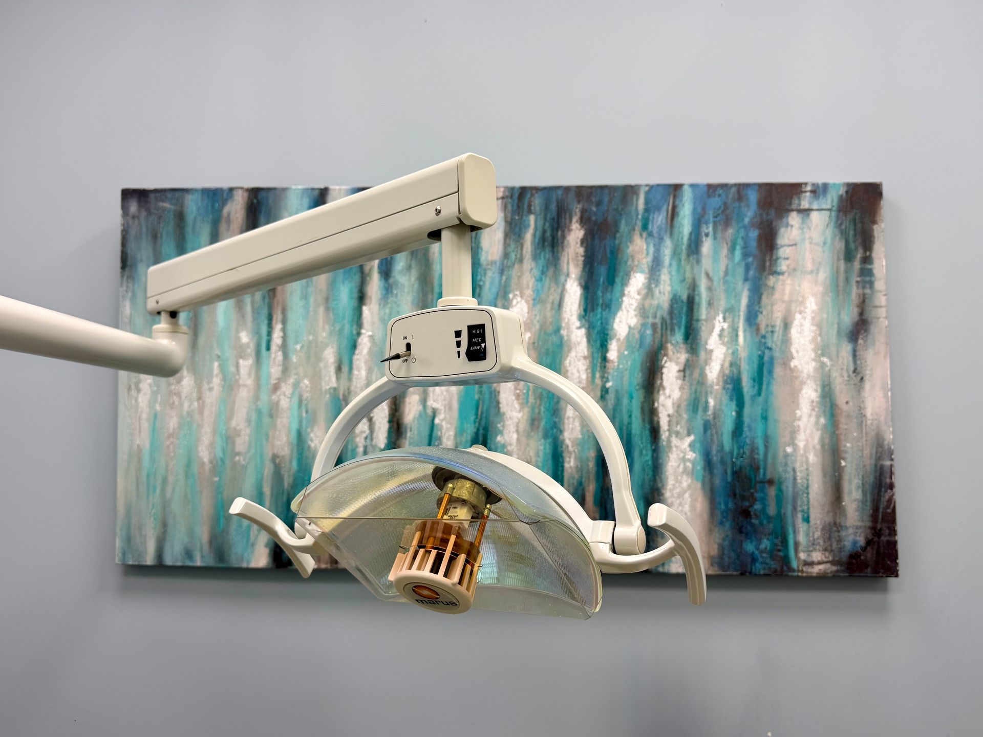 Dental exam light with a curved shield in front of a blue-gray abstract wall panel