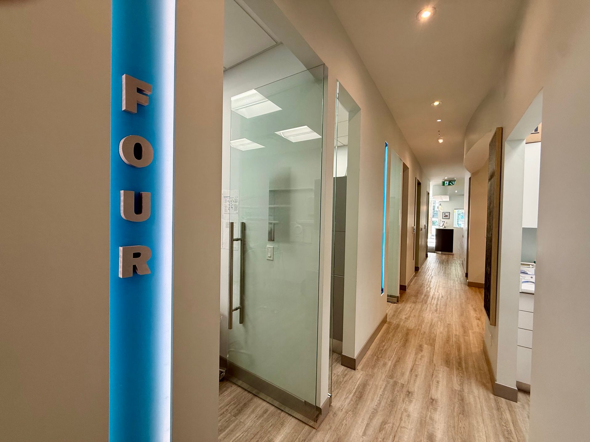 Modern office hallway with glass meeting rooms and a blue “FOUR” sign on the wall