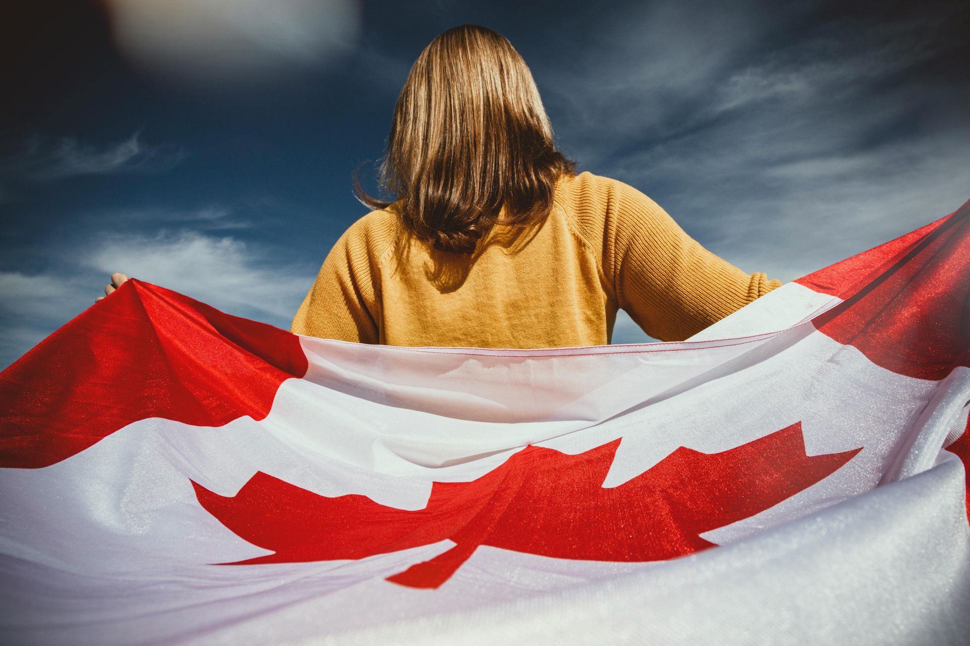 Person holding a large Canadian flag against a cloudy sky