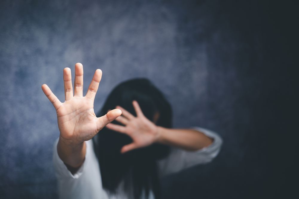 Woman holding hands up, palms forward in a defensive gesture, facing the viewer; blurred background.