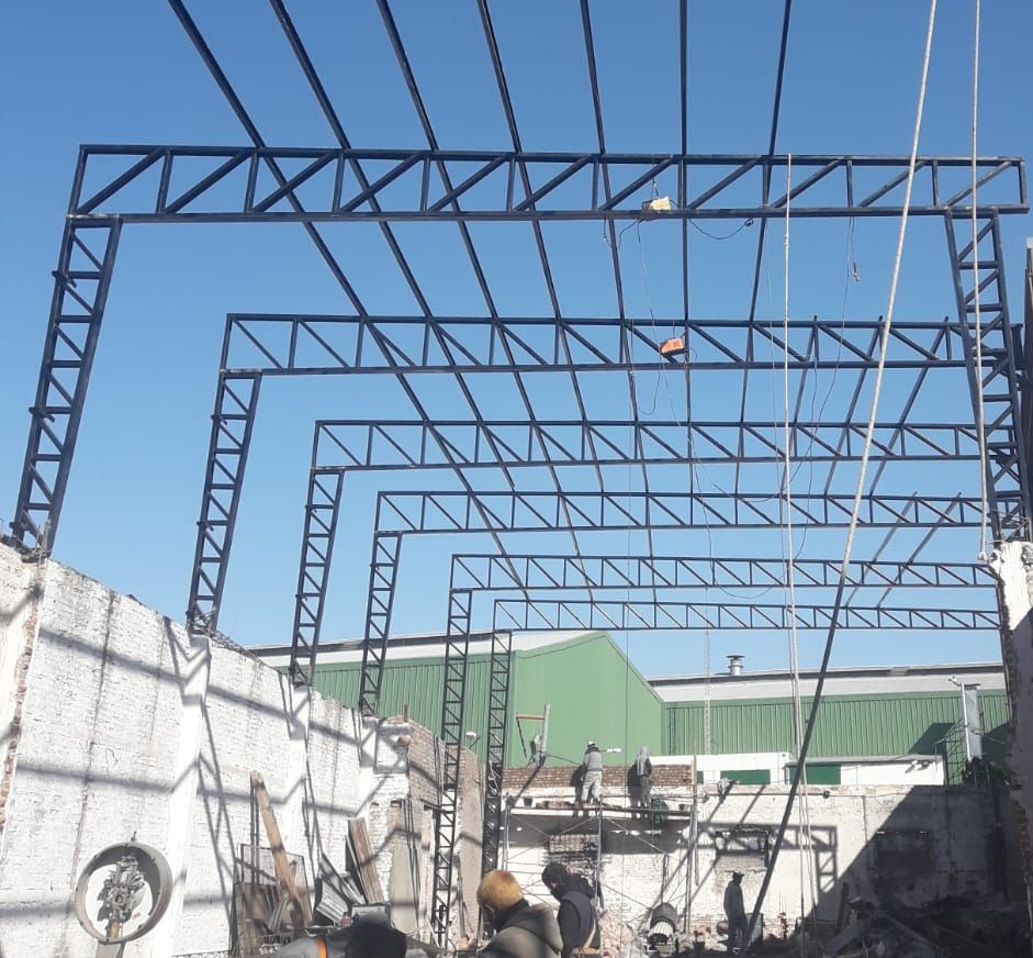 Estructura de acero de un edificio en construcción, con obreros y un cielo azul de fondo.