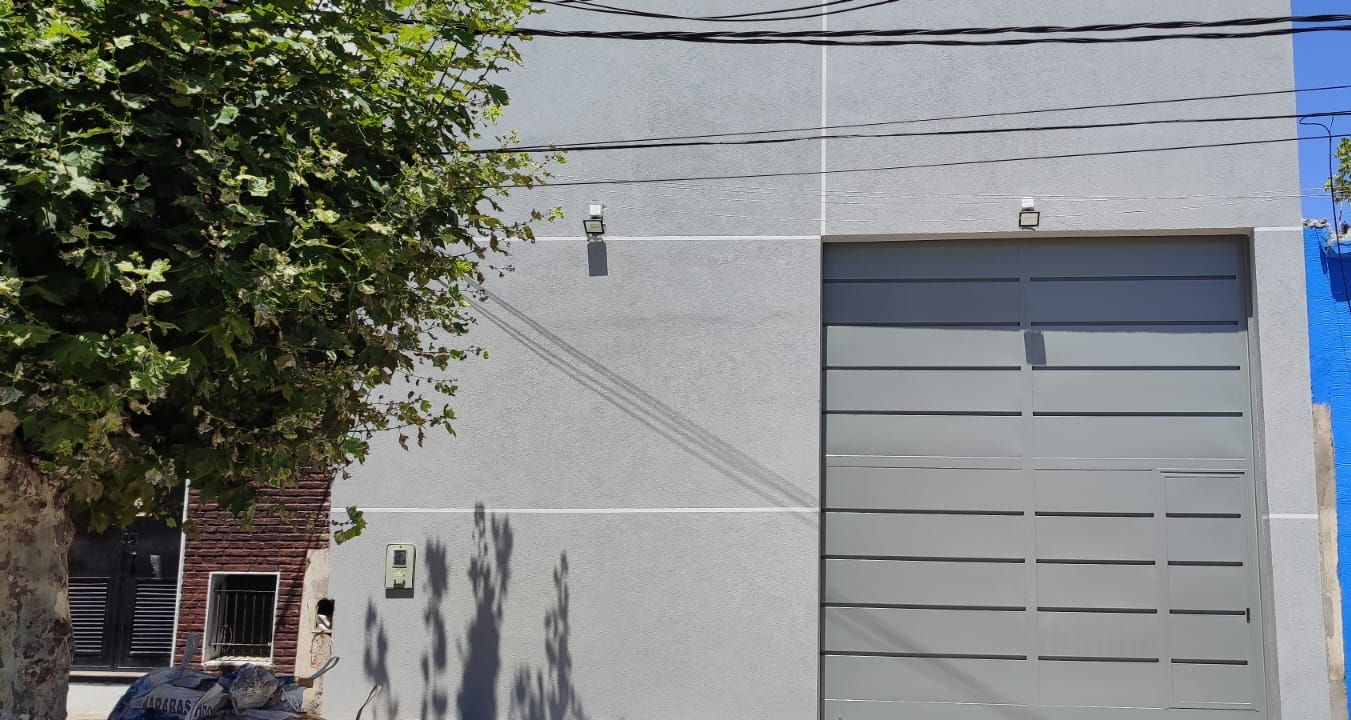 Edificio gris con puerta de garaje gris, cables de electricidad y un árbol a la izquierda.