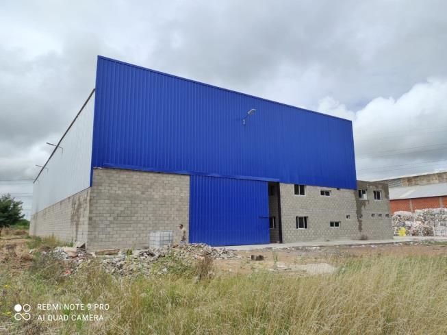 Almacén azul y blanco con una puerta abierta, en un campo de hierba bajo un cielo nublado.