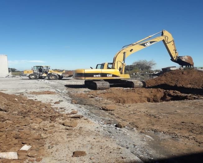 Excavadora amarilla trabajando en la tierra en una obra en construcción; cielo azul.