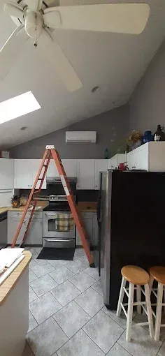A kitchen with white cabinets, stainless steel appliances, a black refrigerator, and an orange ladder in the center.