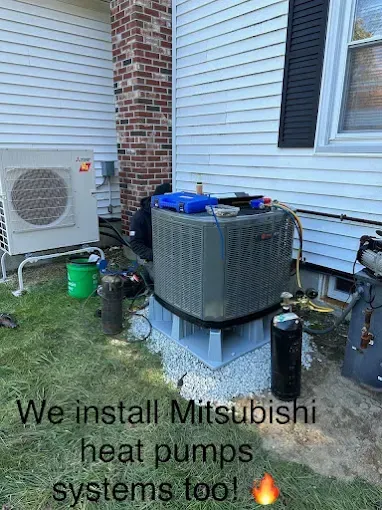 A worker installing a Mitsubishi heat pump system next to an outdoor HVAC unit against a house.